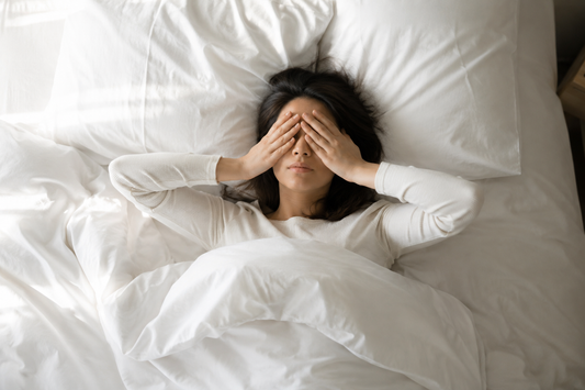 Woman sleeping in bed with her hands covering her eyes.