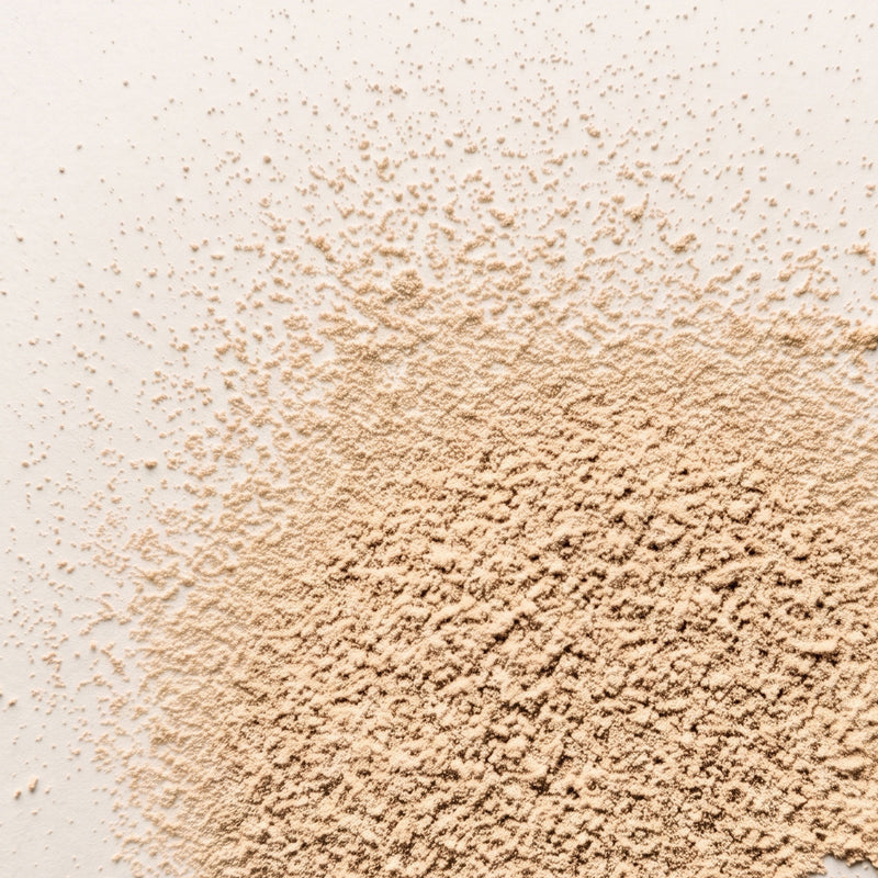 A close-up of loose, finely ground beige powder scattered across a plain white background.