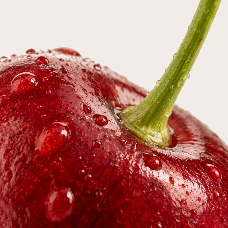Close-up of a glossy red cherry with water droplets and a green stem against a light gray background.